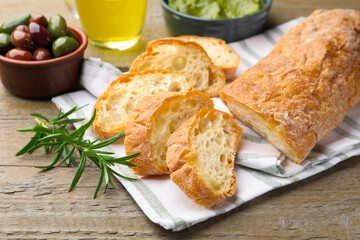 Cut ciabatta, spices and olives on wooden table, closeup