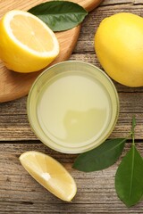 Lemon juice in glass, leaves and fresh lemons on wooden table, flat lay