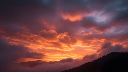 Obraz premium Dramatic sunset sky with vibrant orange and red clouds over a dark mountain silhouette