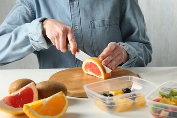 Making fruit salad. Woman cutting grapefruit at white table, closeup