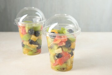 Tasty fruit salad in plastic cups on beige table, closeup