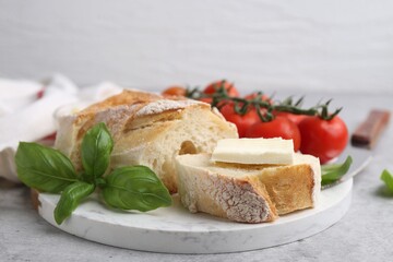 Slices of baguette with butter, basil and tomatoes on light grey table, closeup. Space for text