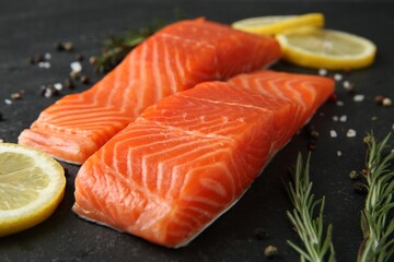 Pieces of salmon fillet, spices and lemon on black table, closeup
