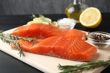 Pieces of salmon fillet, spices and lemon on black wooden table, closeup