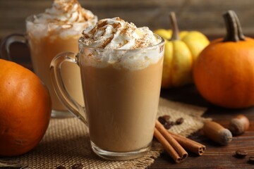Tasty pumpkin latte with whipped cream in glass cups and ingredients on wooden table, closeup