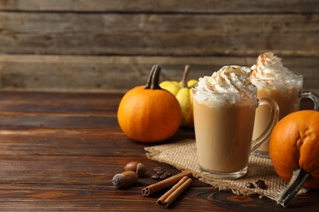 Fototapeta premium Tasty pumpkin latte with whipped cream in glass cups and ingredients on wooden table, closeup. Space for text