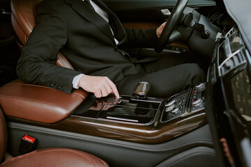 Caucasian middle aged man sitting in luxury car, wearing business suit, operating gear selector...