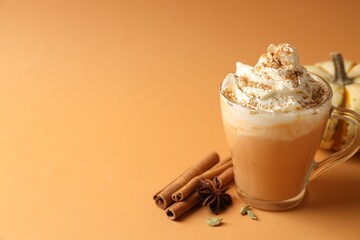 Tasty pumpkin latte with whipped cream, spices and fresh vegetable on orange background, closeup. Space for text