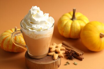Tasty pumpkin latte with whipped cream, spices, cookies and fresh vegetables on orange background, closeup
