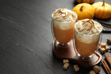 Tasty pumpkin latte with whipped cream, spices and fresh vegetables on black table, closeup. Space for text