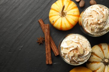 Fototapeta premium Tasty pumpkin latte with whipped cream, spices and fresh vegetables on black table, flat lay. Space for text