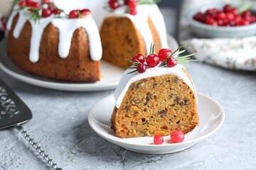 Piece of delicious Christmas cake with icing, cranberries and rosemary on light grey textured table, closeup