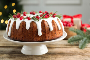Delicious Christmas cake with icing, cranberries and rosemary on wooden table indoors, closeup. Bokeh effect