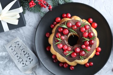 Delicious Christmas cake with chocolate glaze, cranberries, rosemary, server and gift box on grey textured table, flat lay