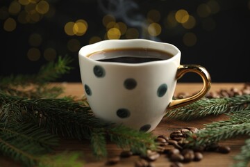 Aromatic coffee in cup, beans and fir tree branches on wooden table against black background with blurred lights, closeup. Bokeh effect
