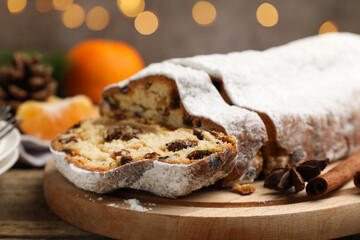 Traditional Christmas Stollen with icing sugar, spices, tangerine and festive decor on wooden table, closeup. Bokeh effect