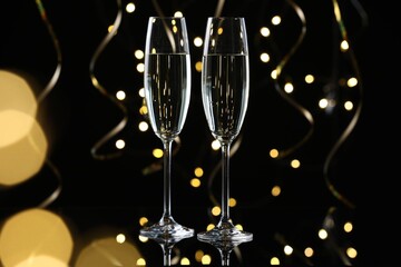 Happy New Year. Sparkling wine in flute glasses and serpentine streamers on black background, bokeh lights