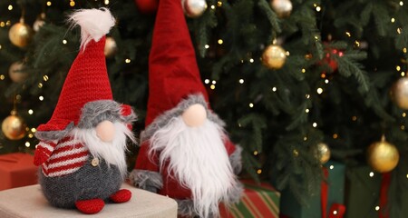 Funny gnomes near Christmas tree and gift boxes in decorated room, closeup. Space for text