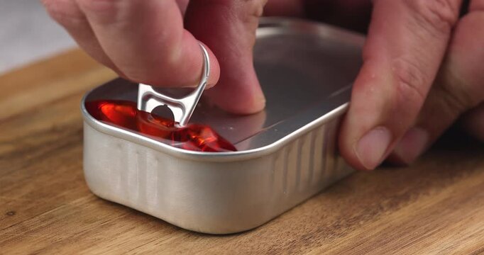 Person opening a can of mussels on a wooden board, close up view showing seafood texture and preserved food concept