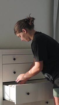 vertical screen white woman inspecting dresser drawer closely, furniture installer checking hardware and drawer glide with concentrated posture, warm sidelight highlighting texture