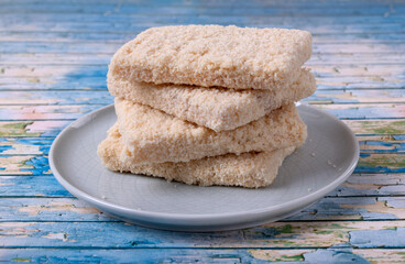 Frozen portioned pollack breaded fillet on a ceramic plate. Four pressed whitefish briquettes in a stack