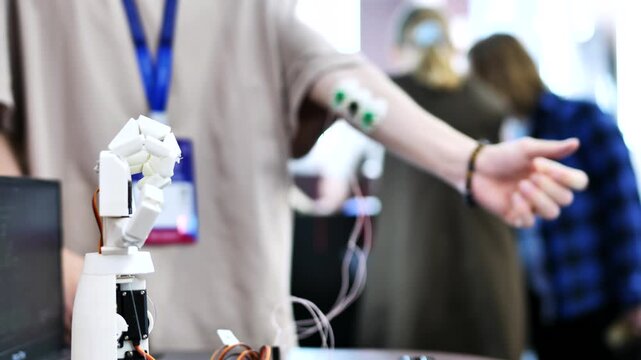 A person controls an artificial robotic arm via wires on their hand.