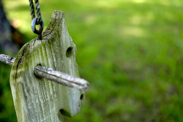 Vintage wooden swing detail with weathered gray wood against blurred green background. Close-up shot capturing nostalgic childhood memories in natural setting.