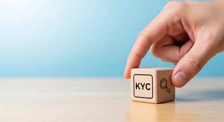 Hand holding a wooden cube with the text KYC and a magnifying glass icon on a wooden table with a blue background, know your customer concept