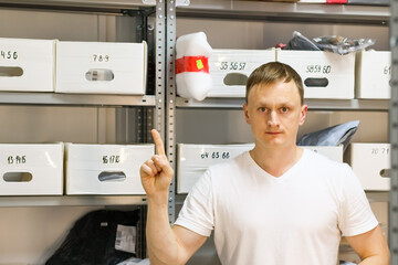 Man in white shirt pointing one finger in front of shelves with numbered boxes. Worker gesturing with one finger at delivery pickup point surrounded by storage shelves