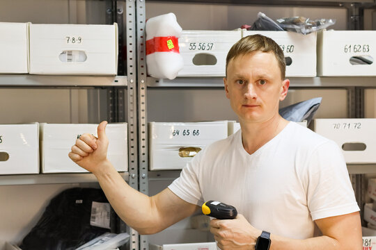Worker thumbs up with scanner in delivery storage. Male worker shows thumbs up holding barcode reader among racks