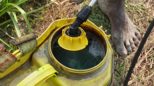 Pesticide or herbicide mixing with water into a yellow sprayer tank in a field