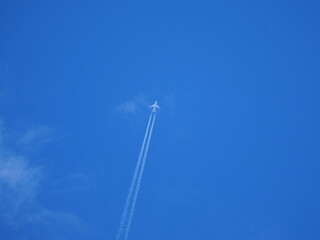 Airplane from below with two white contrails against blue sky. Minimal composition.