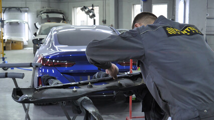 Fototapeta premium A mechanic attaches a plastic bumper guard in a workshop in front of a car brought in for body repair 