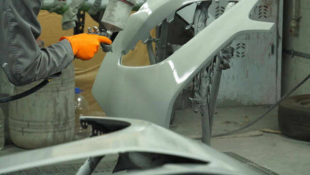 Paint technician spray paints a car front bumper using a paint gun with a diffuser  

