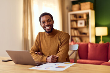 Obraz premium Smiling Man Working on Laptop at Home Office With Charts and Cozy Living Room