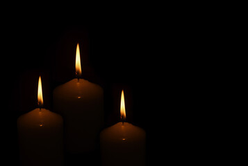 Three burning candles on black