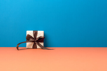 Gift box with brown ribbon on blue and orange background. Merry Christmas, birthday, holiday...