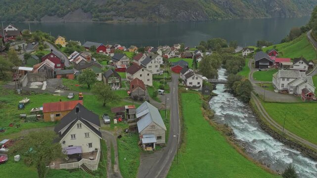 Undredal village sits peacefully by the fjord among towering peaks, drone shot Norway