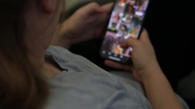 Close up of a young woman at home laying on a couch and scrolling social media, unfocused smartphone screen 