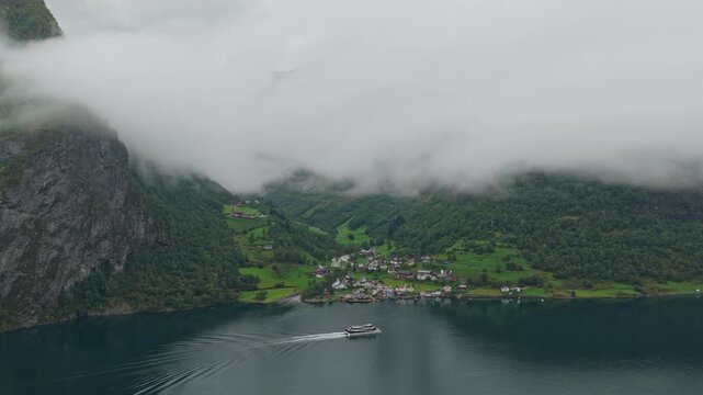 Crowded boat sails through deep fjord near Undredal village, high-angle aerial, Norway