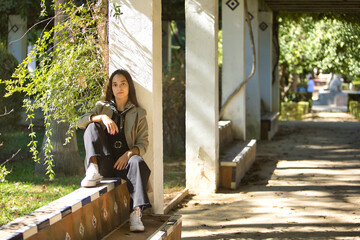 Young woman, brunette, Latina, wearing a jacket, scarf around her neck, and black jeans, looking at...