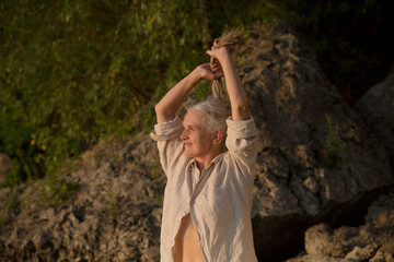 Summer lifestyle portrait senior woman with gray hair relaxes  on the seashore at sunset. Enjoying the little things. spends time in nature in summer.  meditation. banner. greyhairdontcare