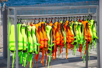 Green and orange Life jackets hanging on a hanger in the port near the boarding of water attractions with the sea in the background