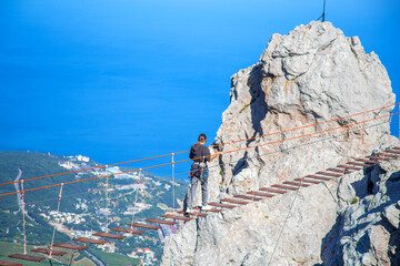 A girl walks along a suspension bridge spanning the battlements of Ai Petri Mountain in Crimea at a great height