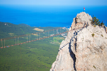 A suspension rope bridge on a high cliff over an abyss with the sea in the background. Extreme Tourist Attraction in the Mountains