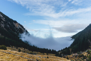 low clouds approaching foggy morning in Carpathians autumn landscape with forest woods and blue sky above 
