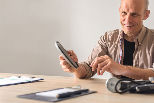Portrait of positive young man with hand expander in clinic for physical therapy. Man showing grip strengthener in physiotherapy consultation