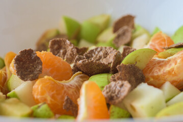 Healthy breakfast with fruit salad and muesli, closeup photo. Bran flakes on top of chopped fruits in bowl, healthy breakfast concept