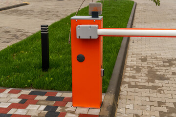 A bright orange security barrier controls access to a parking lot surrounded by green grass and pavement on a sunny day