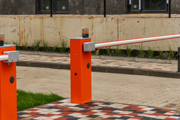 A vibrant orange parking barrier stands at the entrance of a landscaped urban area, highlighting modern design and functionality